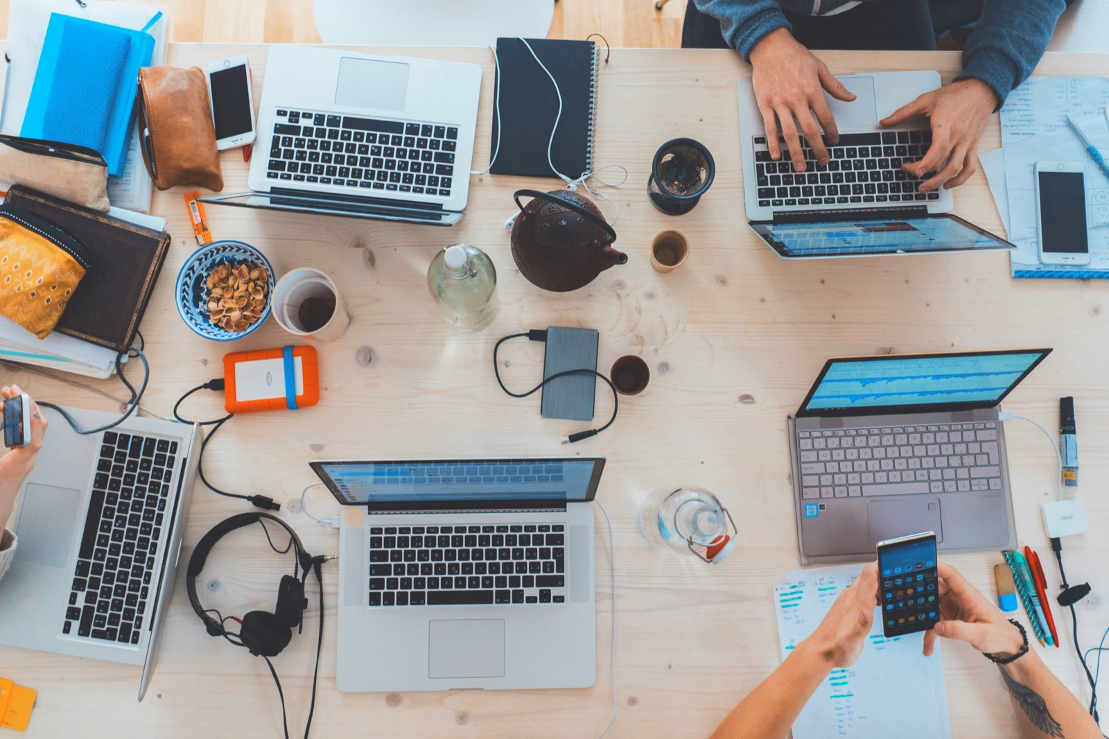 Top-down view of a collaborative workspace with multiple laptops and team members working together at a shared table.