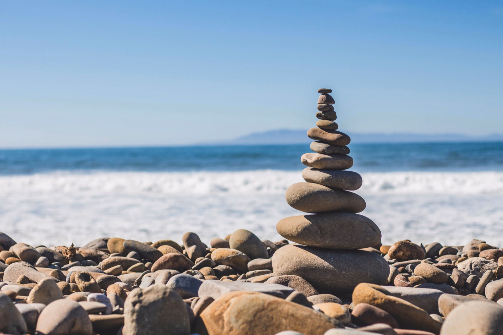 Stacked stone cairn balanced on a pebble beach in front of the ocean, evoking sustainably built recurring revenue tiers.