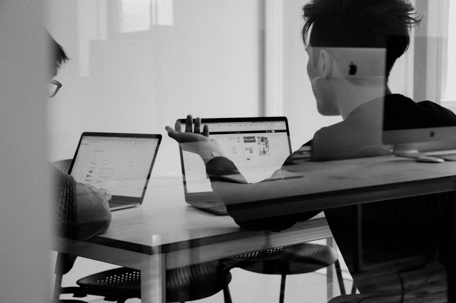 Two creative team members reviewing work on laptops in a modern office, captured in black and white.