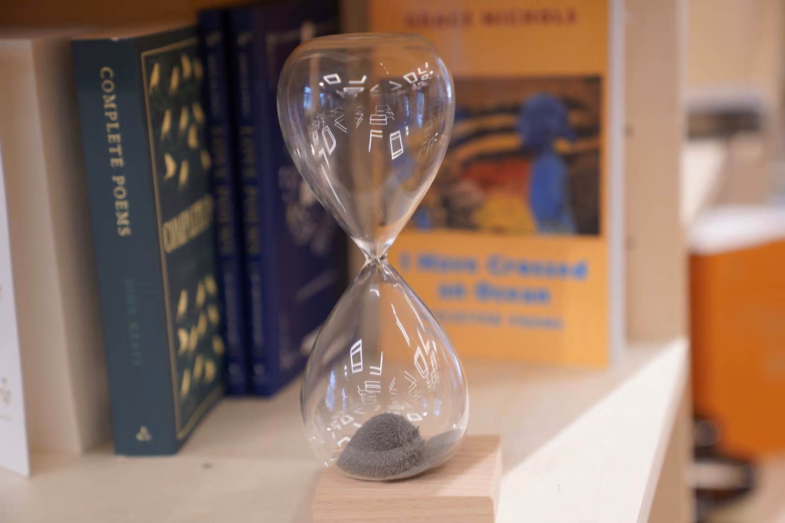 A glass hourglass on a shelf of books — two weeks that compound across six months.